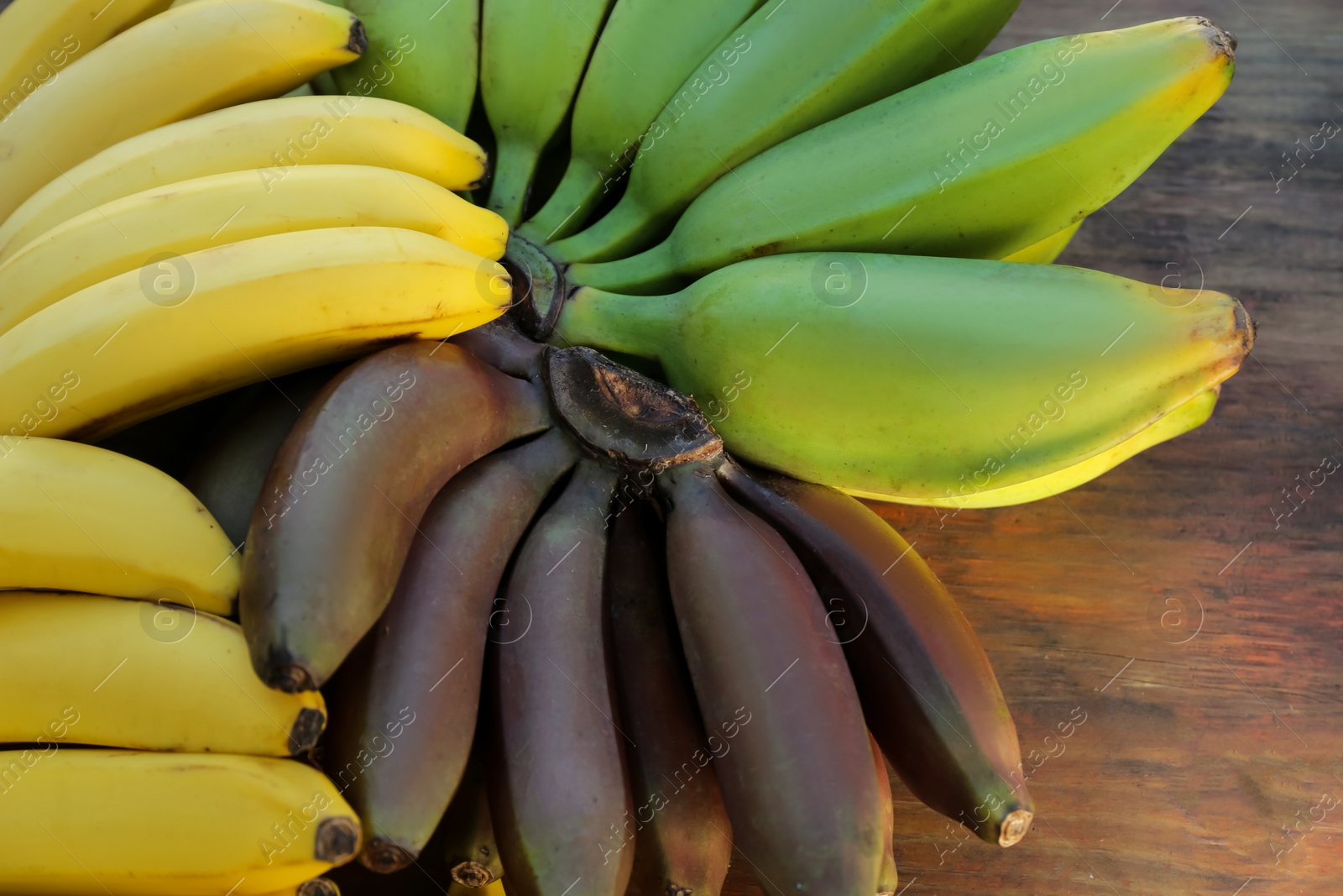 Photo of Different sorts of bananas on wooden table, closeup