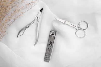 Photo of Manicure scissors, nail clippers and cuticle nipper on white fabric, flat lay
