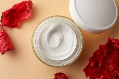 Photo of Jar of face cream and red flower petals on beige background, flat lay