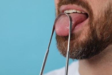 Man brushing his tongue with cleaner on light blue background, closeup. Space for text