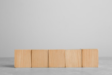 Row of blank wooden cubes on grey table against light background. Space for text