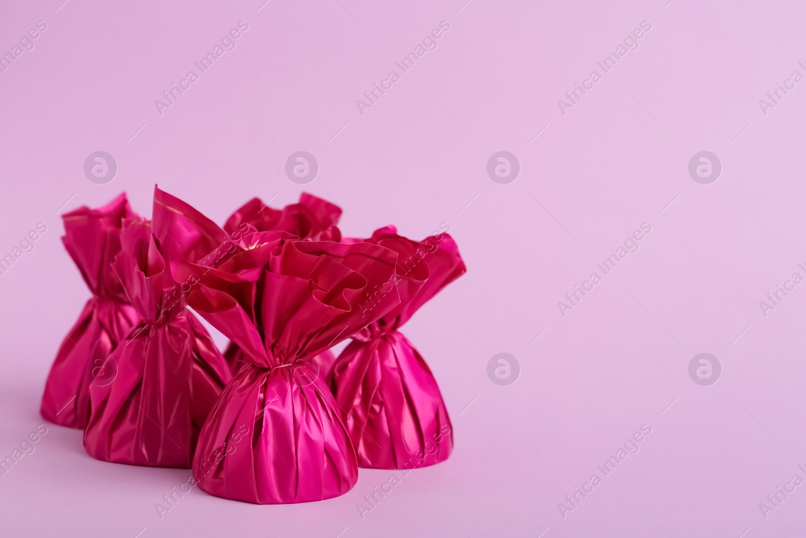 Photo of Candies in bright wrappers on pink background. Space for text