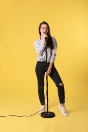 Photo of Young woman wearing casual clothes singing in microphone on color background