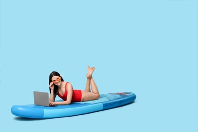Photo of Happy woman with laptop on SUP board against light blue background
