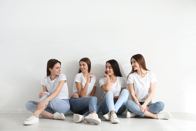 Beautiful young ladies in jeans and white t-shirts near light wall indoors. Woman's Day