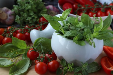 Photo of Mortar with fresh herbs, pepper and cherry tomatoes on wooden table, closeup