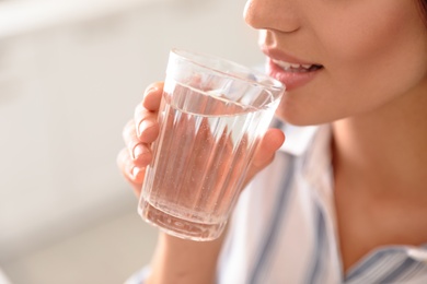 Young woman drinking pure water from glass indoors, closeup
