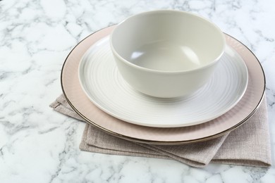 Photo of Clean plates, bowl and napkin on white marble table, closeup. Space for text