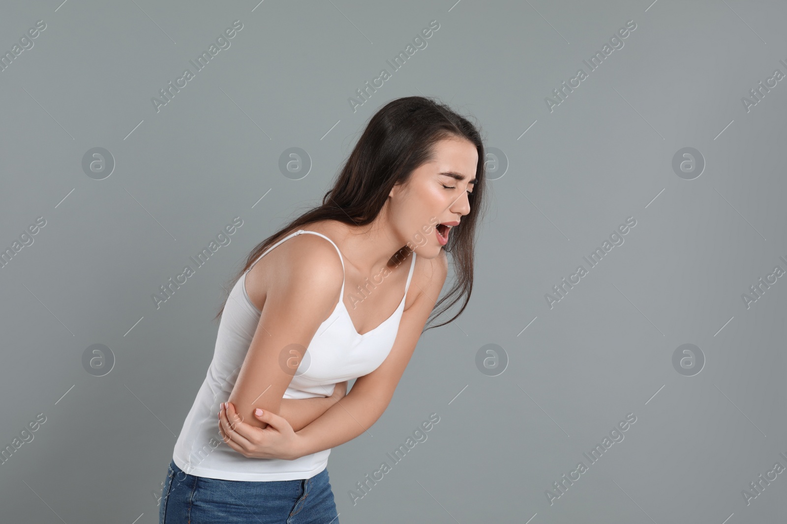 Photo of Young woman suffering from stomach ache on grey background. Food poisoning