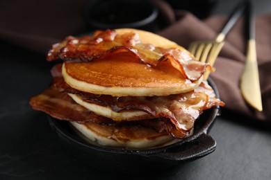 Delicious pancakes with maple syrup and fried bacon on black table, closeup