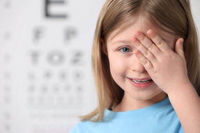 Little girl covering her eye against vision test chart