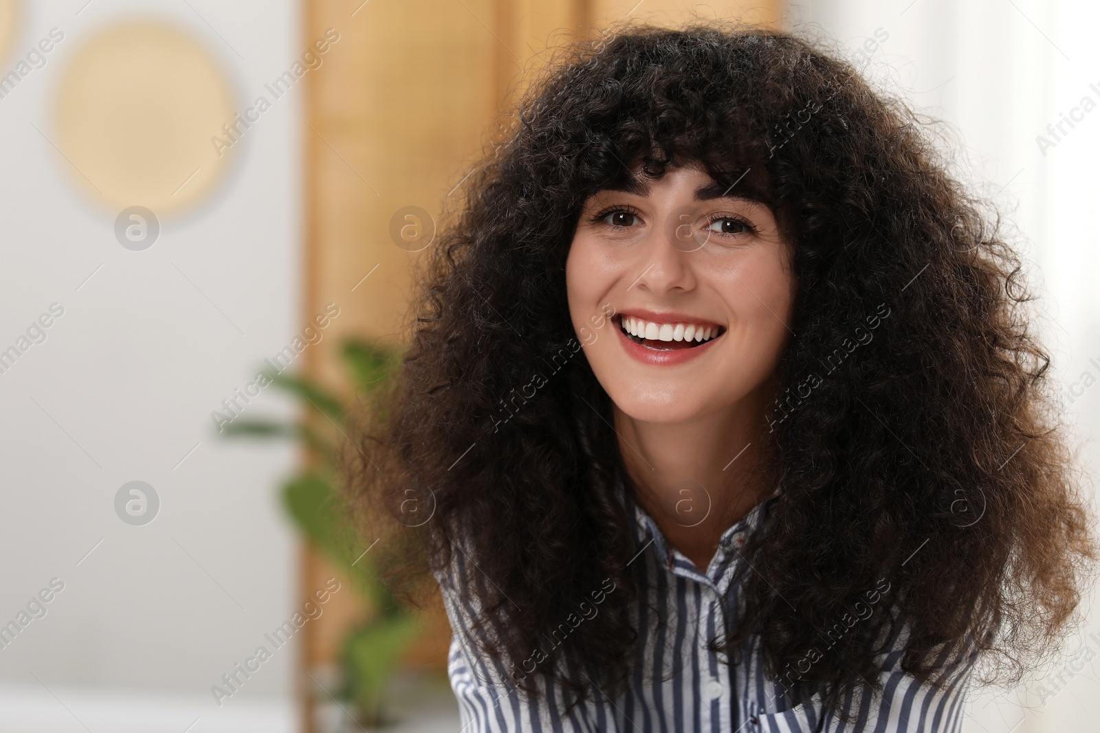 Photo of Portrait of beautiful woman with curly hair indoors. Attractive lady smiling and looking into camera. Space for text