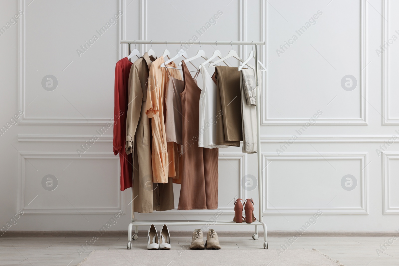 Photo of Rack with different stylish women`s clothes and shoes near white wall indoors