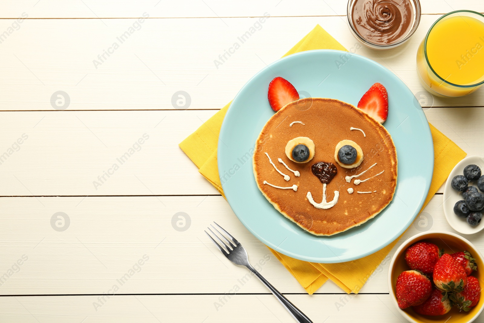 Photo of Creative serving for kids. Plate with cute cat made of pancakes, berries, cream, banana and chocolate paste on white wooden table, flat lay. Space for text
