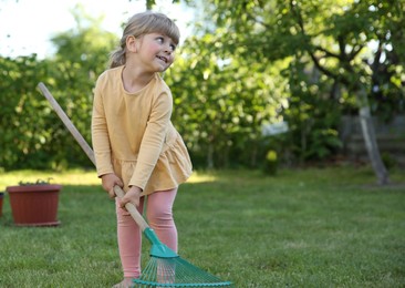 Cute little girl with rake in garden on spring day