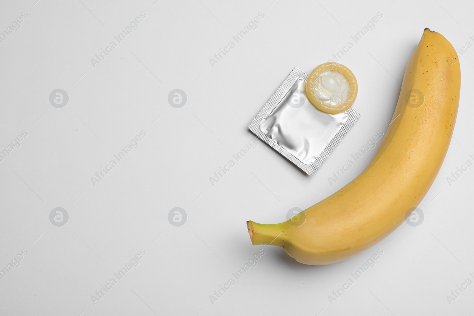 Photo of Condom and banana on white background, top view. Safe sex