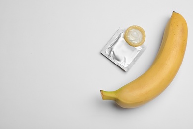 Condom and banana on white background, top view. Safe sex