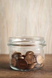 Glass jar with coins on wooden table, closeup