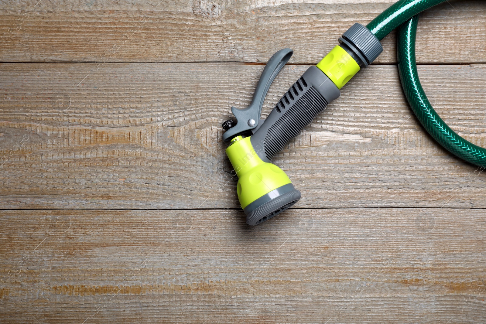 Photo of Green garden hose with spray gun on wooden table, top view. Space for text