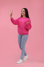 Photo of Smiling young woman taking selfie with smartphone on pink background