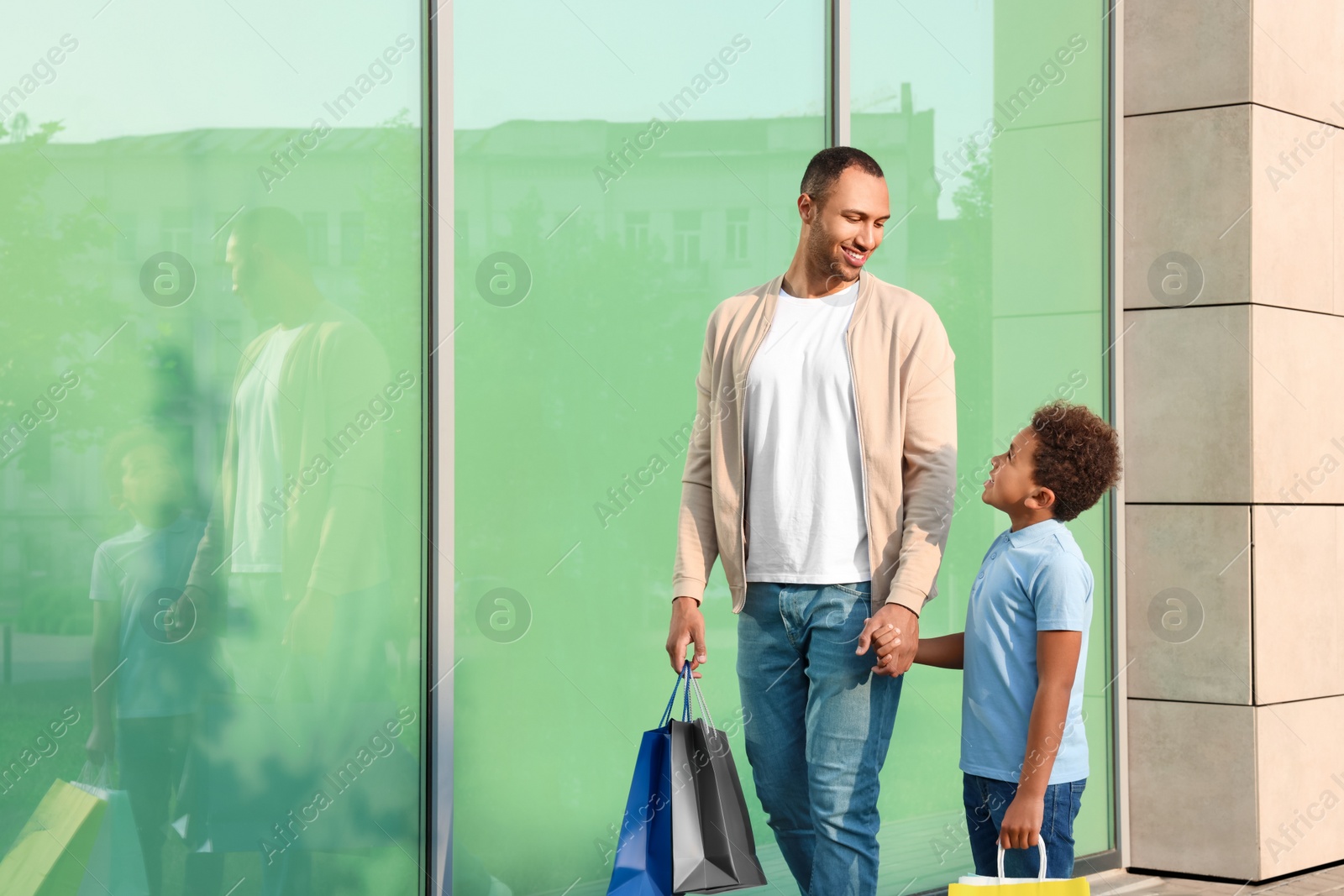 Photo of Family shopping. Happy father and son with colorful bags near mall outdoors