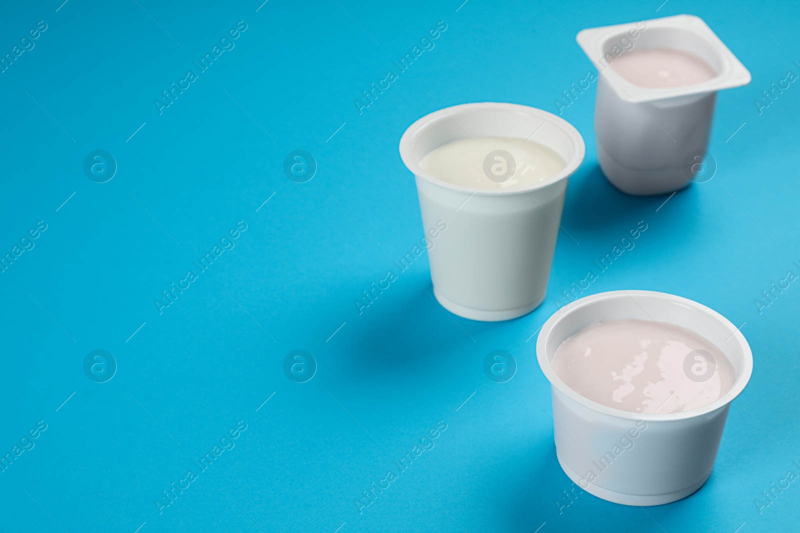 Photo of Plastic cups with tasty yogurt on light blue background, space for text