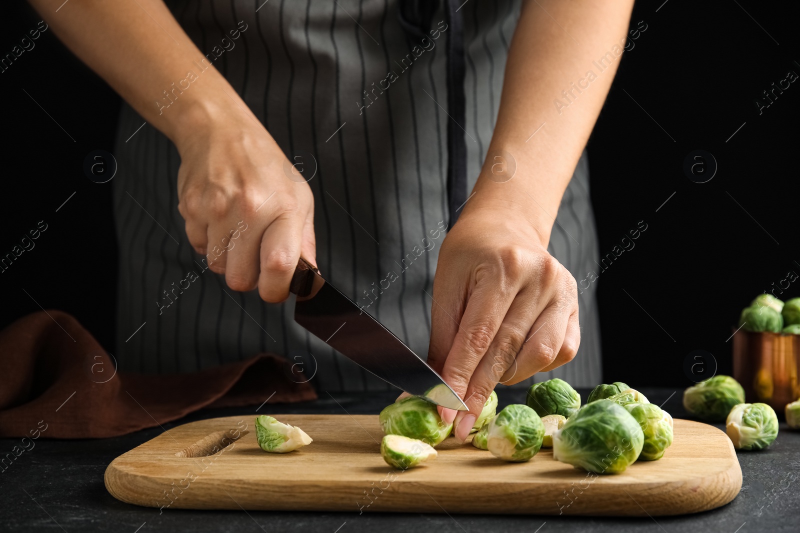 Photo of Woman cutting Brussels sprout at black slate table, closeup