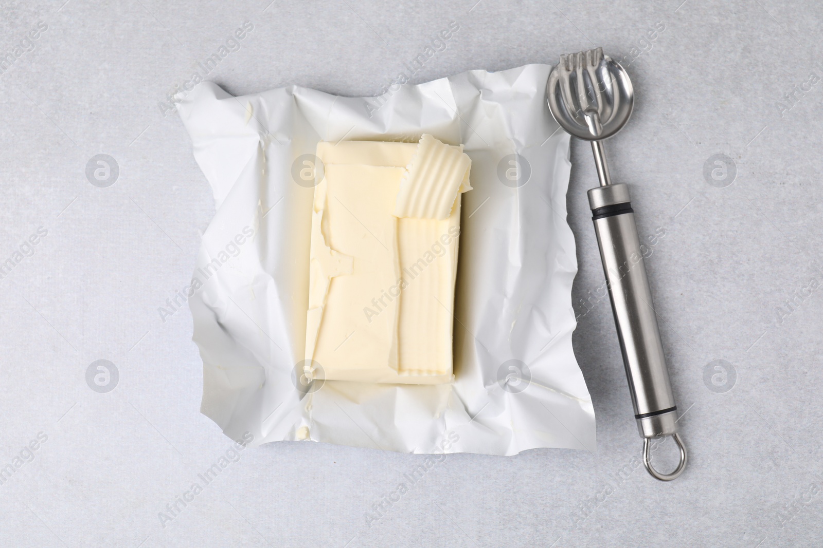 Photo of Tasty butter with curl and spoon on light grey table, top view