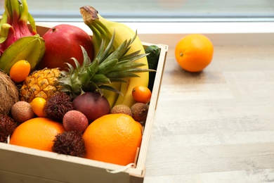 Photo of Assortment of exotic fruits in wooden crate on floor, closeup. Space for text