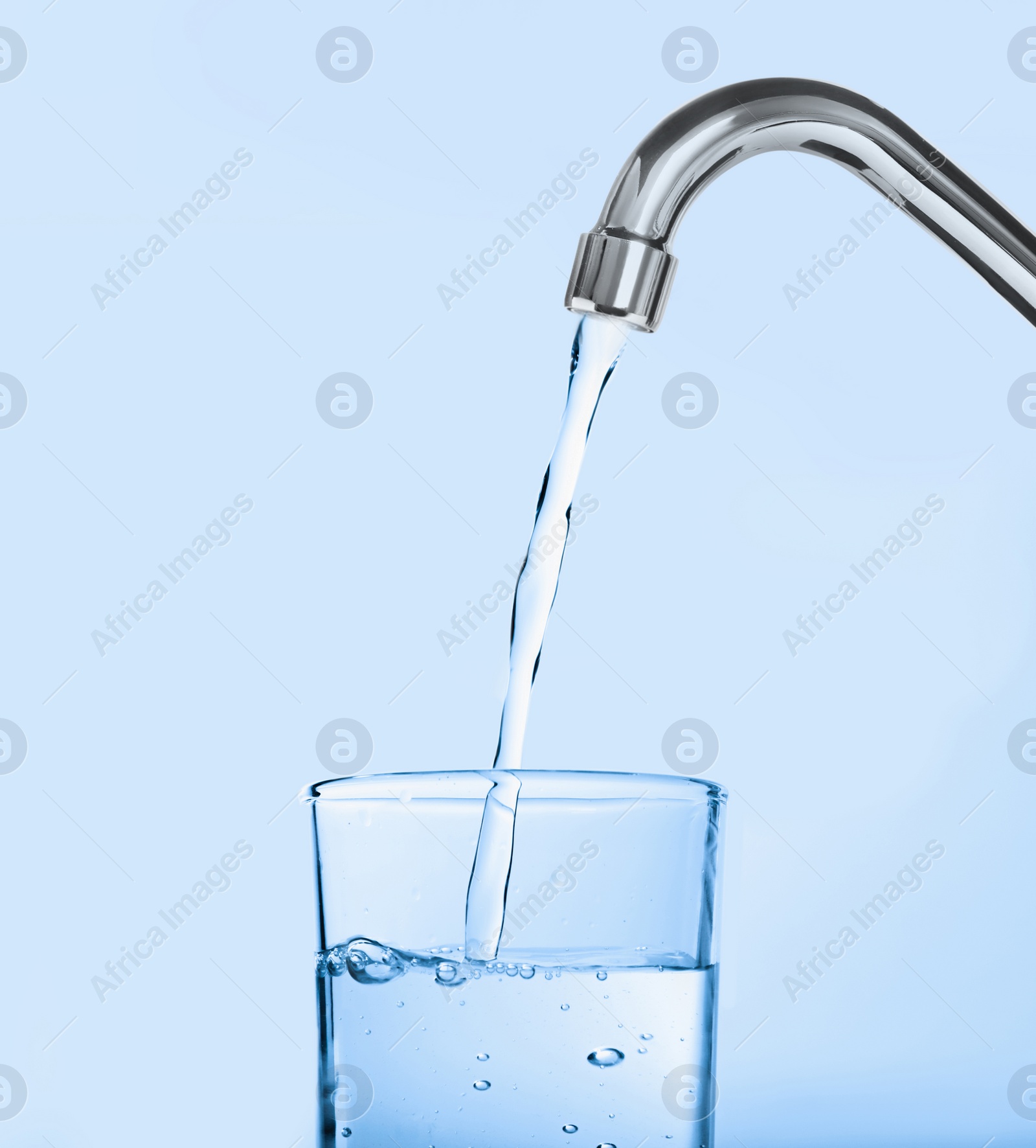 Image of Filling glass with water from tap on light blue background