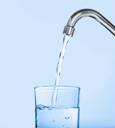Image of Filling glass with water from tap on light blue background
