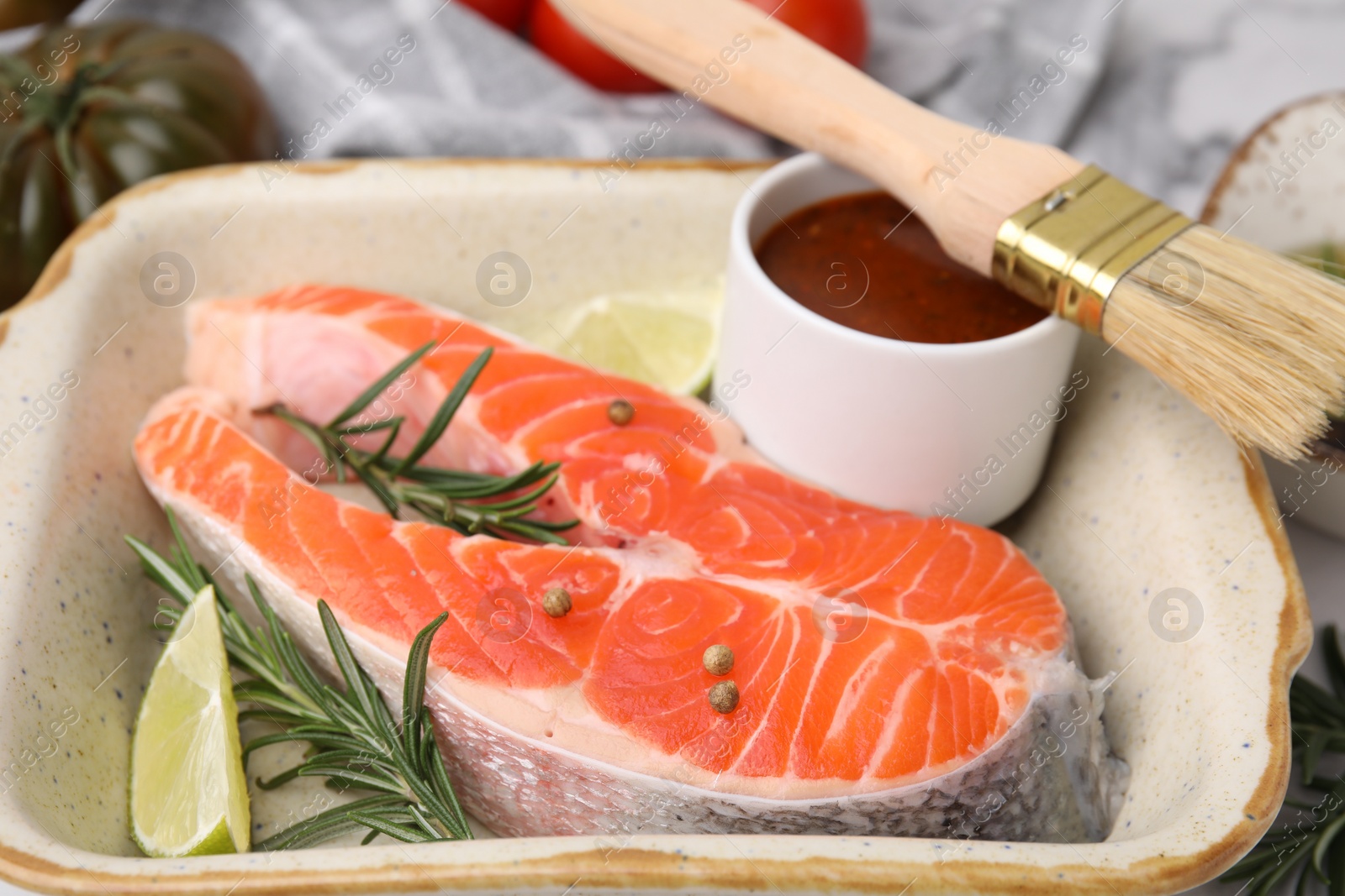 Photo of Fresh fish, lime, rosemary and marinade in baking dish on table, closeup