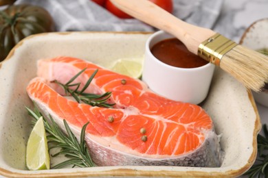 Fresh fish, lime, rosemary and marinade in baking dish on table, closeup