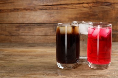 Glasses of different refreshing soda water with ice cubes on wooden table. Space for text