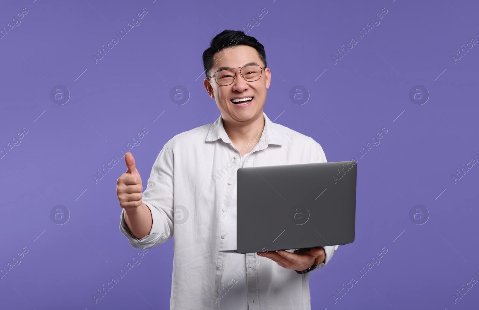 Photo of Happy man with laptop showing thumb up gesture on lilac background