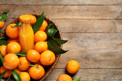 Photo of Basket with fresh tangerines and bottle of juice on wooden table, flat lay. Space for text