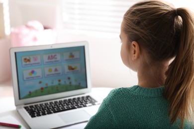 Photo of Little girl learning English indoors at online lesson, back view