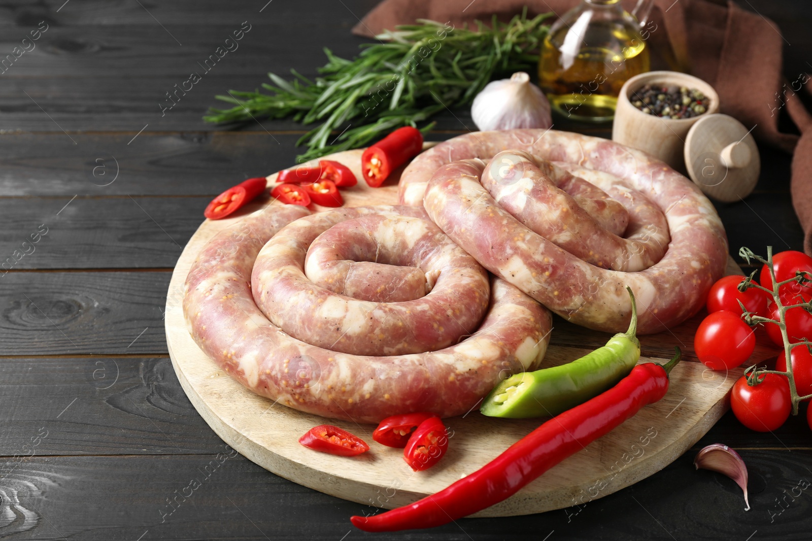 Photo of Raw homemade sausages, spices and other products on dark wooden table, closeup