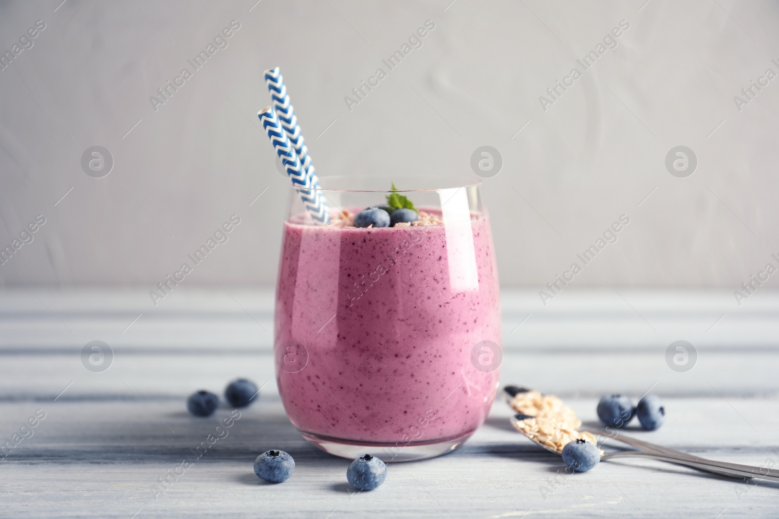 Photo of Tasty blueberry smoothie in glass, berries and oatmeal on wooden table