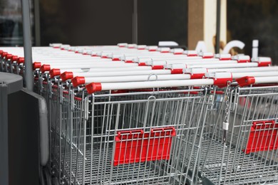 Many empty metal shopping carts near supermarket outdoors