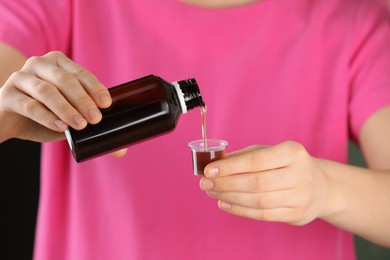 Photo of Woman pouring cough syrup into measuring cup, closeup
