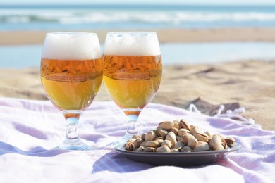 Photo of Glasses of cold beer and pistachios on sandy beach near sea
