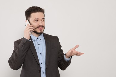 Happy man in suit talking on smartphone against light grey background. Space for text