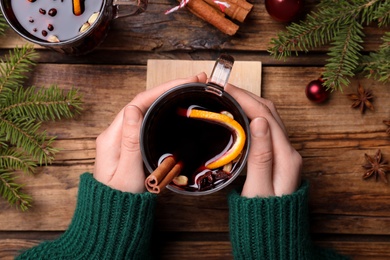 Photo of Woman with cup of mulled wine at wooden table, top view