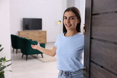 Photo of Happy woman welcoming near door. Invitation to come indoors