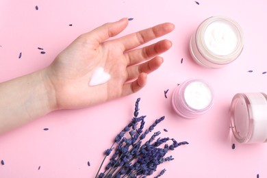 Photo of Woman applying hand cream and lavender flowers on pink background, top view