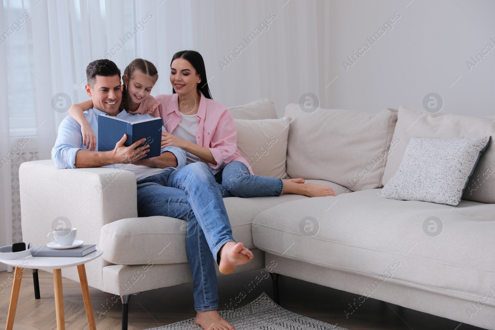 Photo of Father reading book to family on sofa in living room