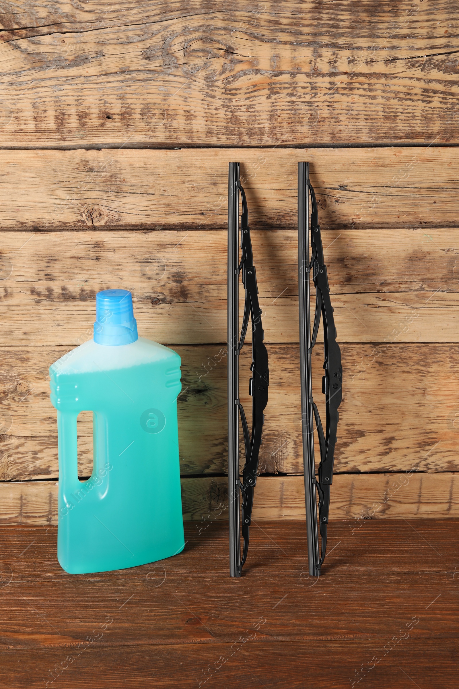 Photo of Bottle of windshield washer fluid and wipers on wooden table