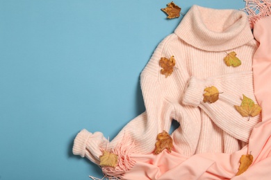 Photo of Pink sweater, scarf and dry leaves on light blue background, flat lay with space for text. Autumn season