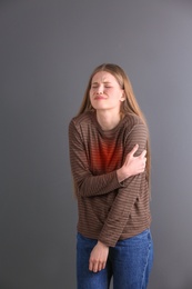 Young woman having heart attack on gray background